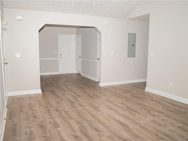 spare room with arched walkways, a textured ceiling, baseboards, light wood-style floors, and electric panel