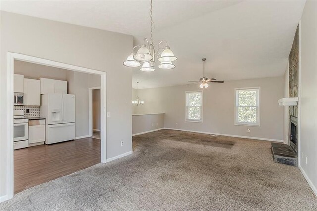 unfurnished living room featuring a large fireplace, carpet, baseboards, lofted ceiling, and ceiling fan with notable chandelier