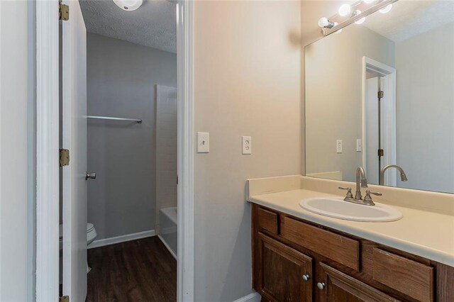 bathroom with vanity, toilet, baseboards, a textured ceiling, and wood finished floors