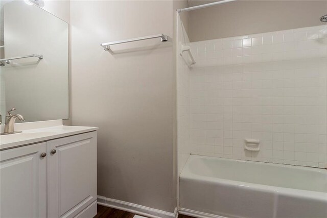 full bath with washtub / shower combination, baseboards, wood finished floors, and vanity