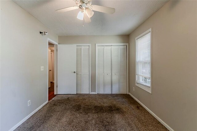 unfurnished bedroom featuring baseboards, multiple closets, a ceiling fan, and carpet