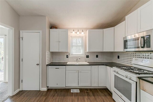 kitchen with a sink, dark wood finished floors, dark countertops, white appliances, and visible vents