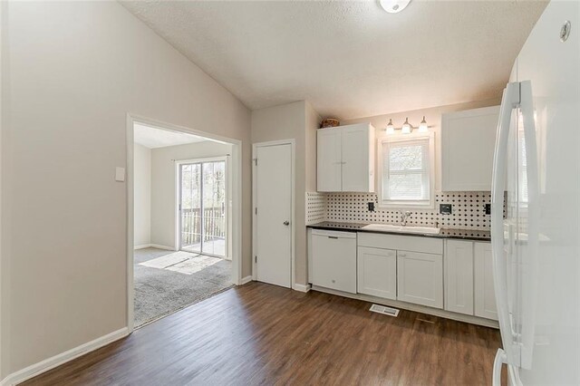 kitchen with lofted ceiling, plenty of natural light, dark countertops, and white appliances