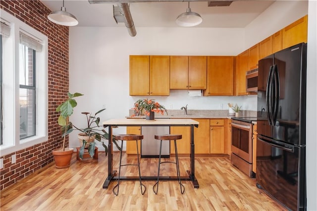 kitchen with stainless steel appliances, brick wall, light wood-type flooring, and hanging light fixtures