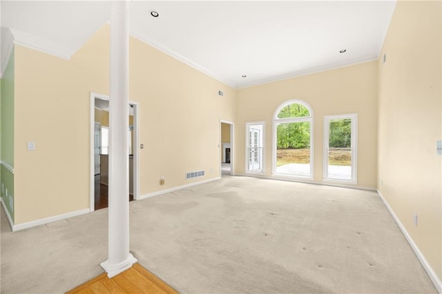 unfurnished living room with visible vents, a high ceiling, baseboards, ornamental molding, and carpet