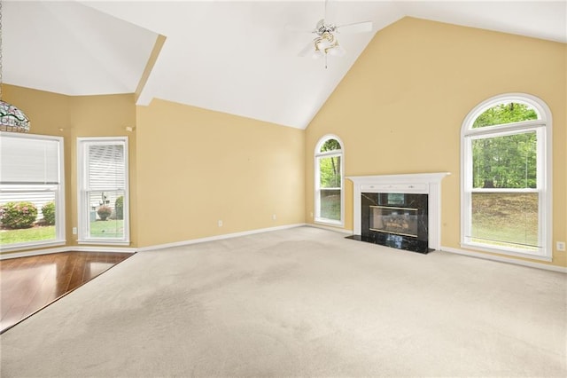 unfurnished living room with carpet floors, baseboards, high vaulted ceiling, a high end fireplace, and a ceiling fan