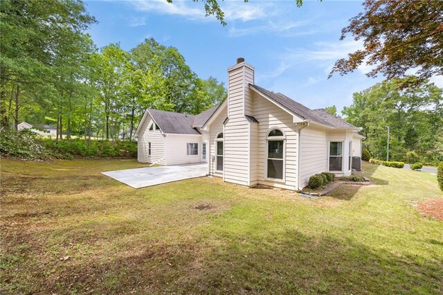 back of house with a patio, a shingled roof, a lawn, and a chimney