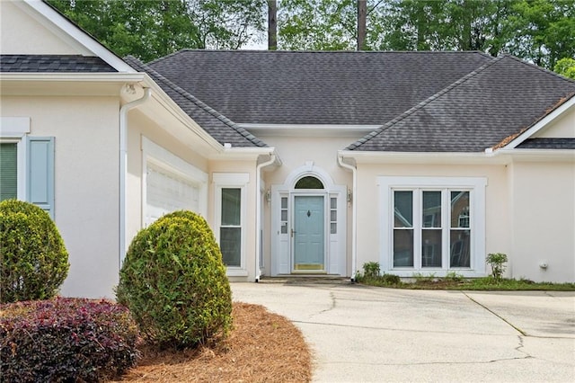 property entrance with roof with shingles, stucco siding, and a garage