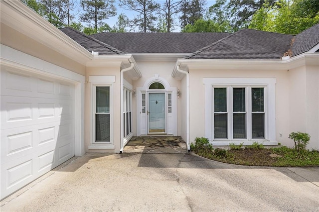 property entrance featuring a garage, a shingled roof, concrete driveway, and stucco siding