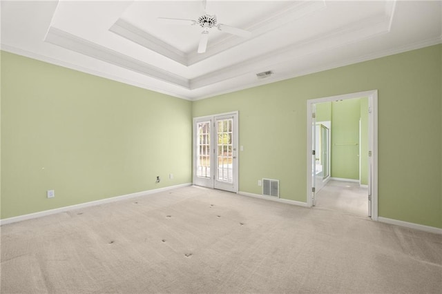 empty room featuring light colored carpet, a tray ceiling, visible vents, and ornamental molding