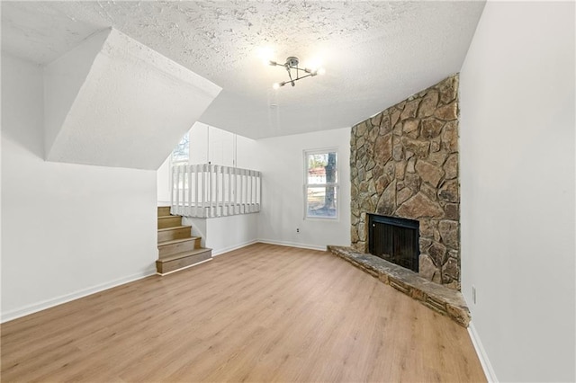 unfurnished living room featuring a textured ceiling, light hardwood / wood-style floors, and a stone fireplace