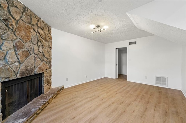 unfurnished living room featuring visible vents, a stone fireplace, a textured ceiling, and light wood-style flooring