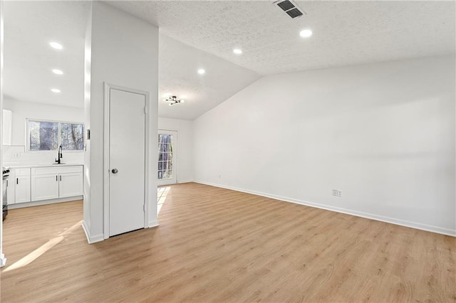 unfurnished living room with a textured ceiling, sink, light hardwood / wood-style floors, and vaulted ceiling