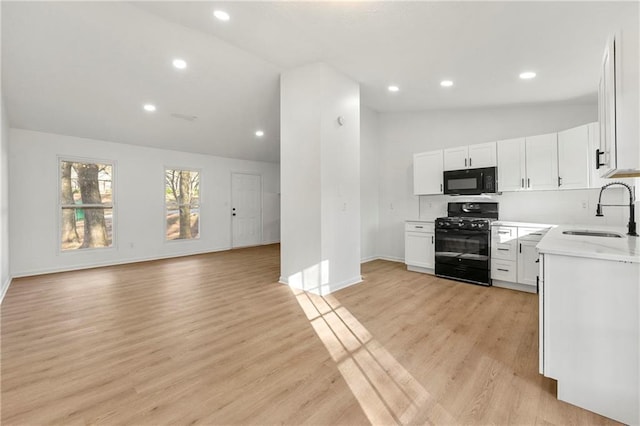 kitchen with black appliances, white cabinetry, open floor plan, and a sink