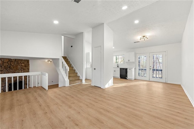 unfurnished living room featuring lofted ceiling, recessed lighting, light wood-style floors, french doors, and stairway