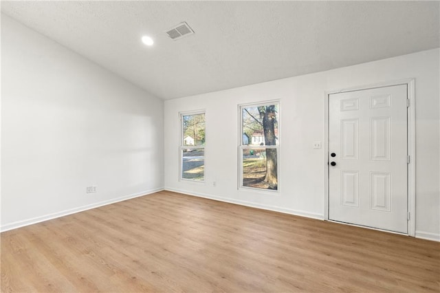 empty room with vaulted ceiling, light wood-style flooring, visible vents, and baseboards