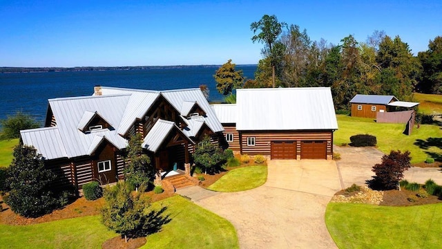 cabin with metal roof, a chimney, a water view, a front lawn, and concrete driveway