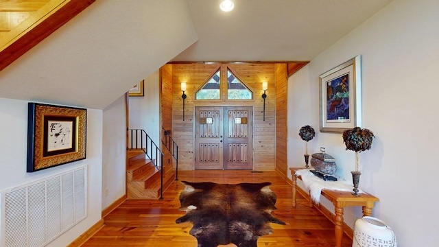 entryway featuring wood finished floors, stairs, baseboards, vaulted ceiling, and wood walls