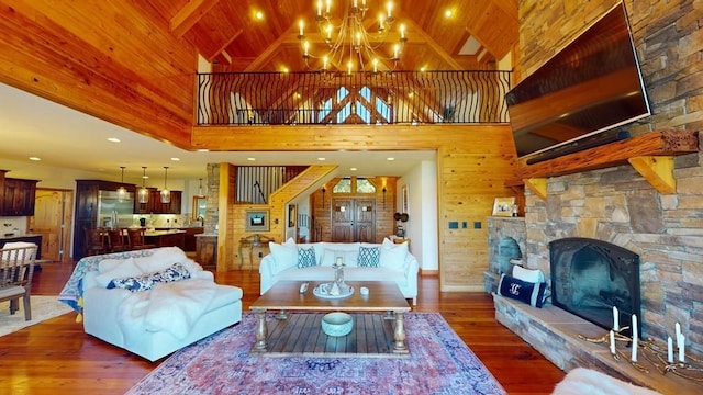 living room featuring a chandelier, wood finished floors, high vaulted ceiling, and a stone fireplace