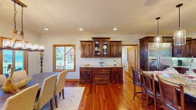 kitchen featuring built in refrigerator, hanging light fixtures, recessed lighting, wood finished floors, and glass insert cabinets