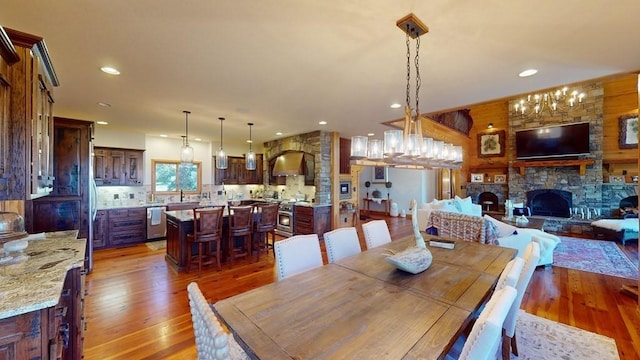 dining space with light wood-type flooring, a stone fireplace, recessed lighting, and a chandelier