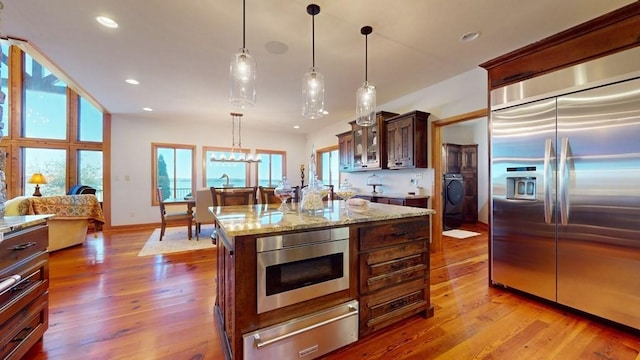 kitchen with stainless steel built in refrigerator, a warming drawer, washer / dryer, glass insert cabinets, and wood finished floors