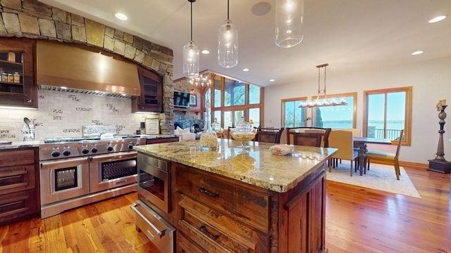 kitchen with appliances with stainless steel finishes, ventilation hood, a warming drawer, tasteful backsplash, and light wood-type flooring