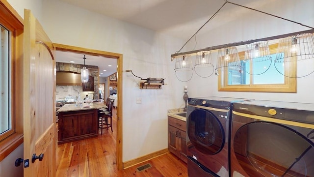 laundry area with washer and dryer, light wood finished floors, cabinet space, and baseboards