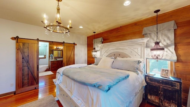 bedroom with a chandelier, a barn door, wood finished floors, wooden walls, and recessed lighting