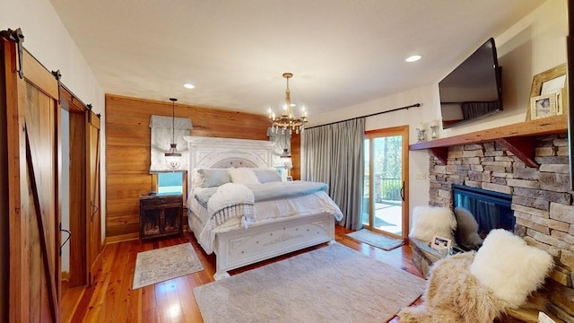 bedroom featuring access to outside, a stone fireplace, a chandelier, a barn door, and wood finished floors