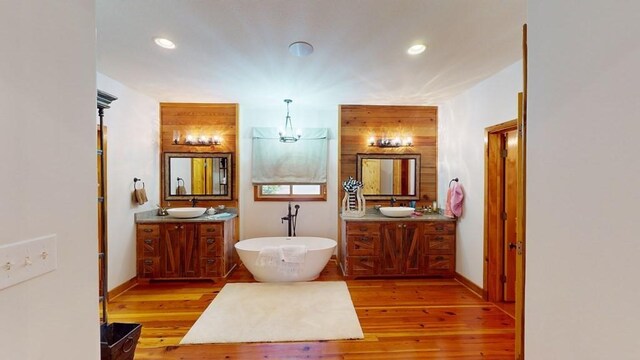 bathroom featuring wood finished floors, a freestanding tub, two vanities, recessed lighting, and a chandelier