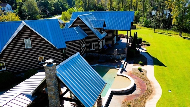 rear view of property with metal roof, a pool, a lawn, and a patio area
