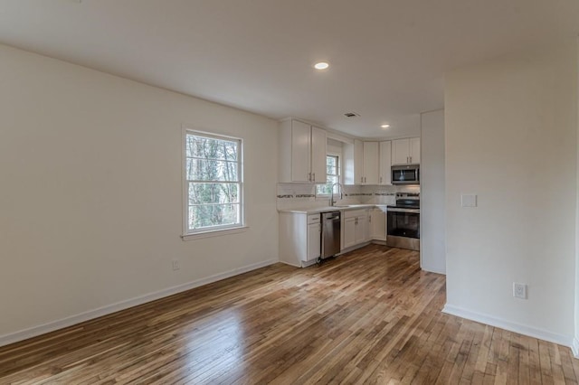 kitchen with sink, light hardwood / wood-style flooring, appliances with stainless steel finishes, white cabinets, and backsplash