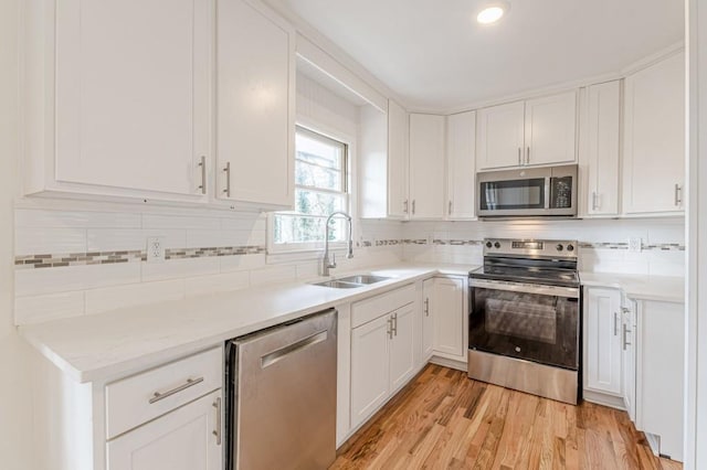 kitchen featuring appliances with stainless steel finishes, white cabinetry, sink, backsplash, and light hardwood / wood-style flooring