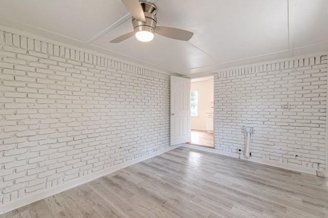 spare room with ceiling fan, brick wall, and light wood-type flooring