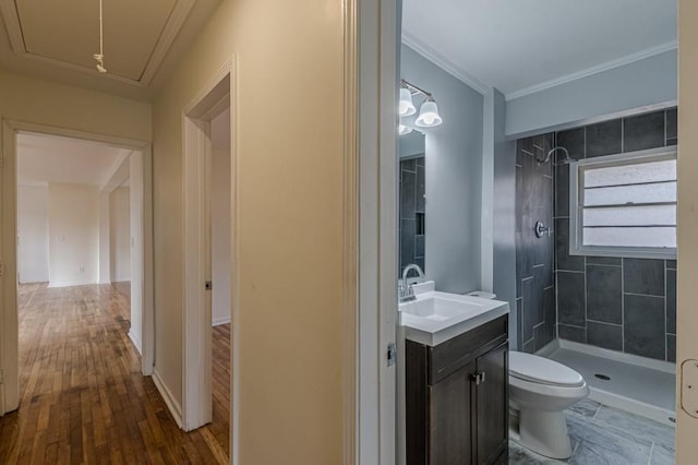 bathroom with a tile shower, hardwood / wood-style flooring, vanity, toilet, and crown molding