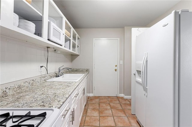 kitchen with light stone countertops, backsplash, sink, white refrigerator with ice dispenser, and white cabinets