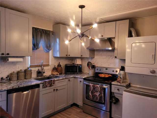 1625 Conley Rd Unit 229, Conley, GA 30288 - kitchen featuring appliances with stainless steel finishes, estacked washer and dryer, wall chimney range hood, light stone counters, and wood finished floors