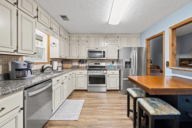 kitchen featuring a sink, visible vents, appliances with stainless steel finishes, light stone countertops, and light wood finished floors