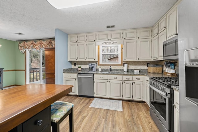 kitchen with appliances with stainless steel finishes, decorative backsplash, visible vents, and light wood-style floors