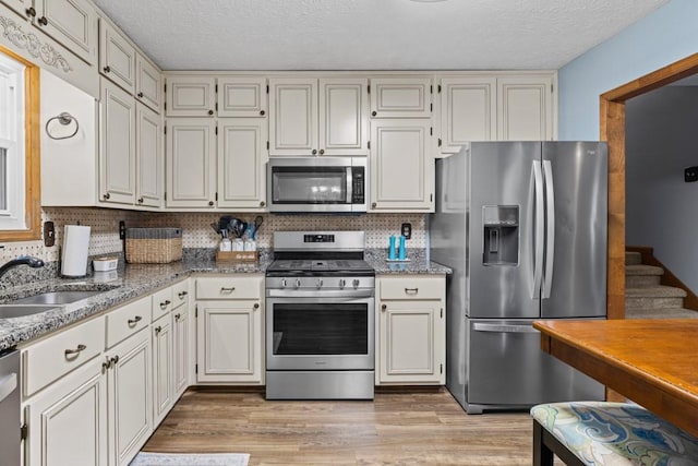 kitchen featuring tasteful backsplash, light wood-style flooring, appliances with stainless steel finishes, light stone countertops, and a sink