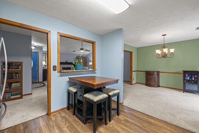 dining area with a textured ceiling, a notable chandelier, carpet flooring, wood finished floors, and baseboards