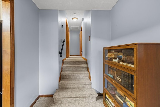 stairway with carpet flooring, a textured ceiling, and baseboards