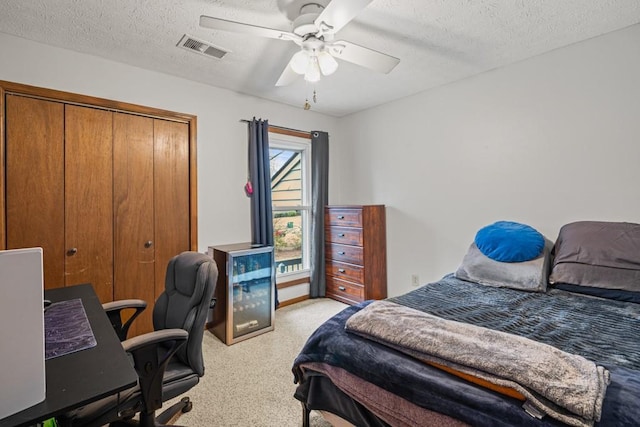 bedroom with a textured ceiling, light colored carpet, a ceiling fan, visible vents, and a closet