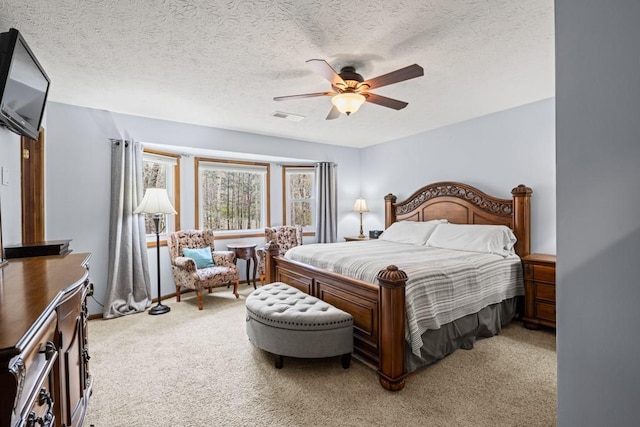 bedroom featuring a ceiling fan, light colored carpet, visible vents, and a textured ceiling