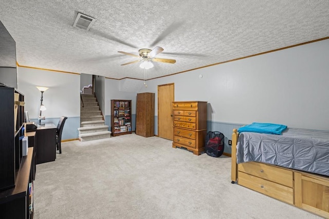 carpeted bedroom with a textured ceiling, visible vents, crown molding, and wainscoting