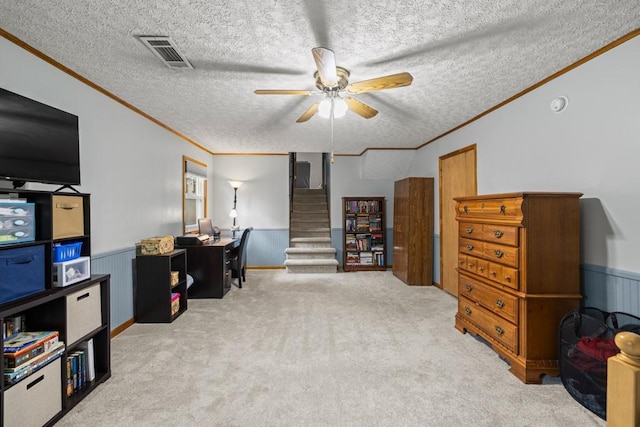 carpeted office with a wainscoted wall, crown molding, visible vents, ceiling fan, and a textured ceiling