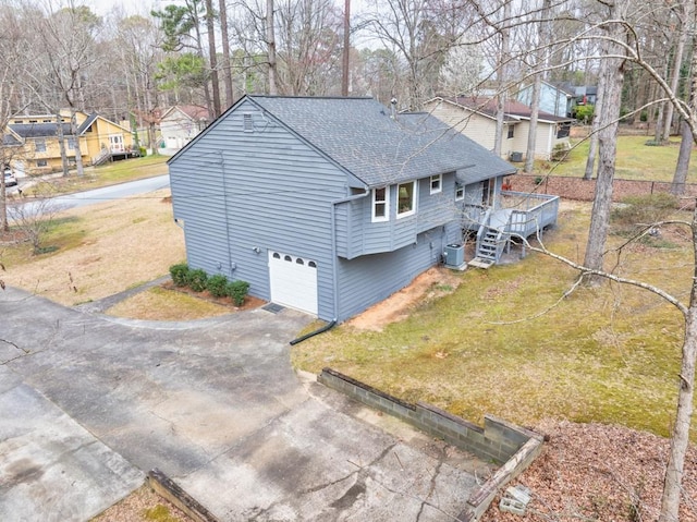 exterior space with central air condition unit, a shingled roof, a front yard, a garage, and driveway