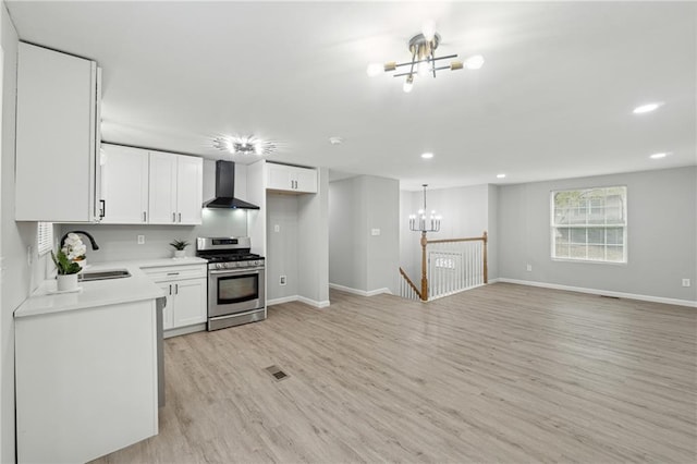 kitchen with white cabinetry, sink, wall chimney exhaust hood, light hardwood / wood-style flooring, and stainless steel range with gas stovetop