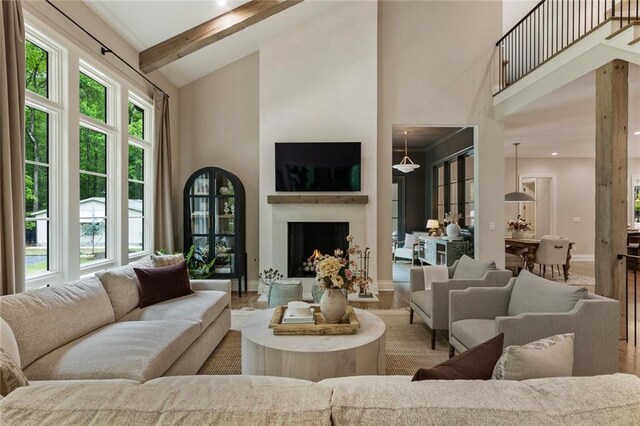 living room featuring a warm lit fireplace, beam ceiling, high vaulted ceiling, baseboards, and wood finished floors